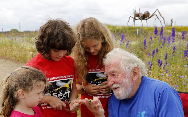 David Bellamy smiling talking to children about an insect he is holding.