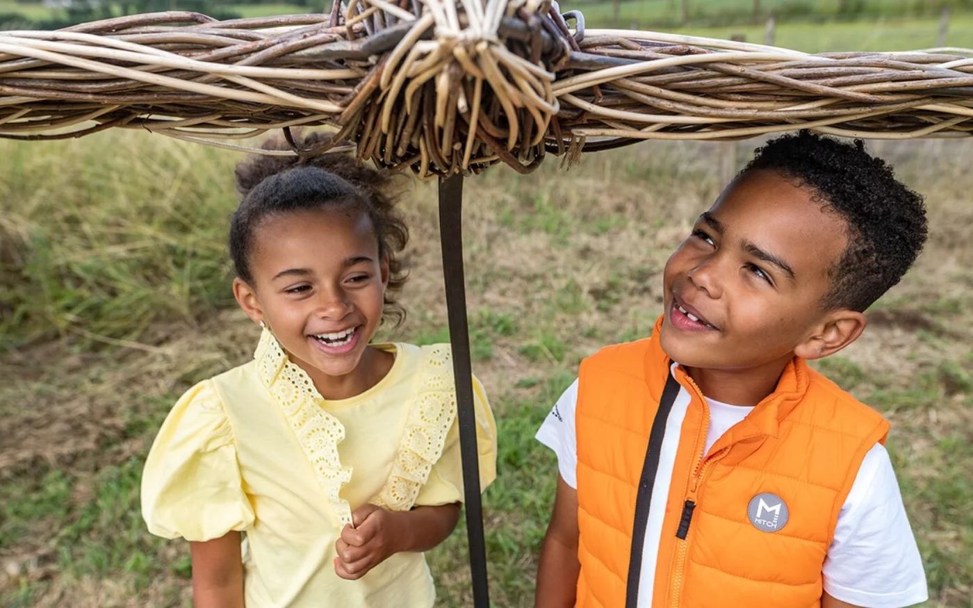 Two children standing under a wicker model