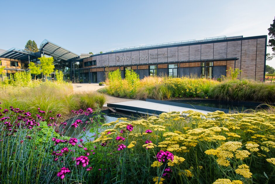 Building with 'RHS Hilltop The home of gardening science' written, behind a pond and garden with flowers